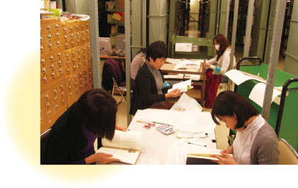 4人の女性が図書館で書籍を調べている写真。机の上は資料でいっぱい。