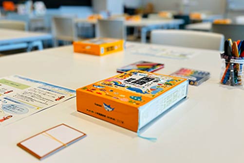 机の上に国語辞典、かるたの札、カラフルなマーカーが準備してある写真