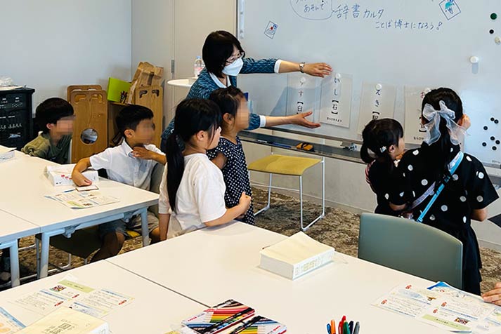 ホワイトボードにことばのシートを貼る柏野先生と問題に取り組むこどもたち